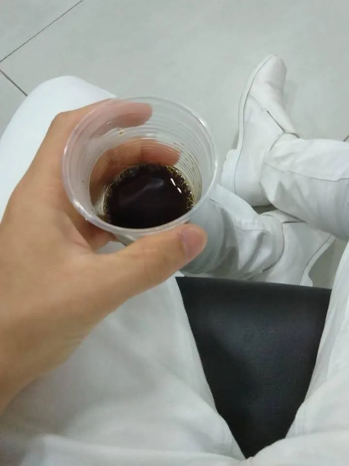 Café em copo plástico durante um plantão de enfermagem, com o uniforme branco de Thalles Diamantino ao fundo