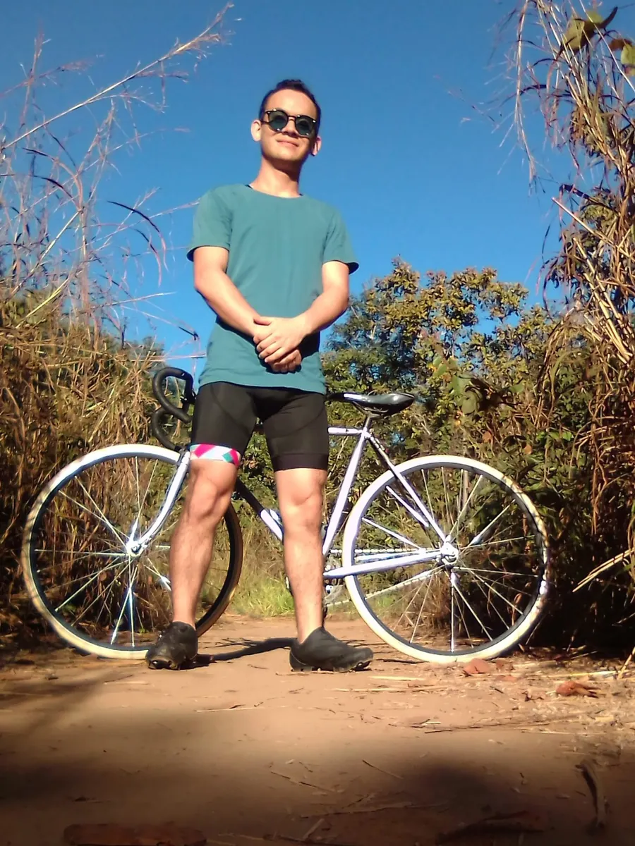 Thalles Diamantino de óculos escuros ao lado da bicicleta, numa estrada de terra sob céu azul