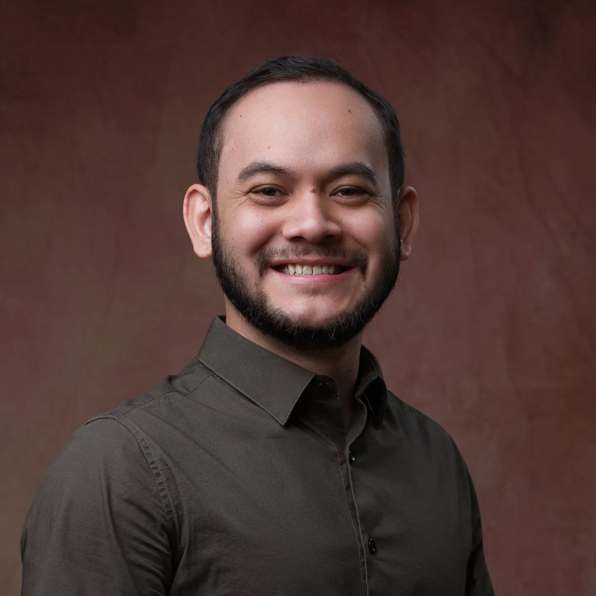 Retrato de Thalles Diamantino sorrindo, de camisa escura, sobre fundo marrom