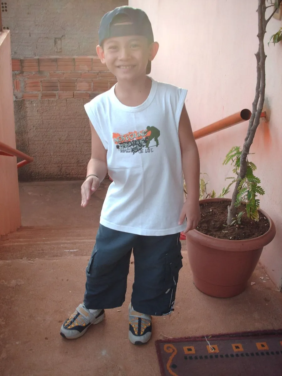 Thalles Diamantino ainda criança, de boné e sorrindo, na varanda de casa