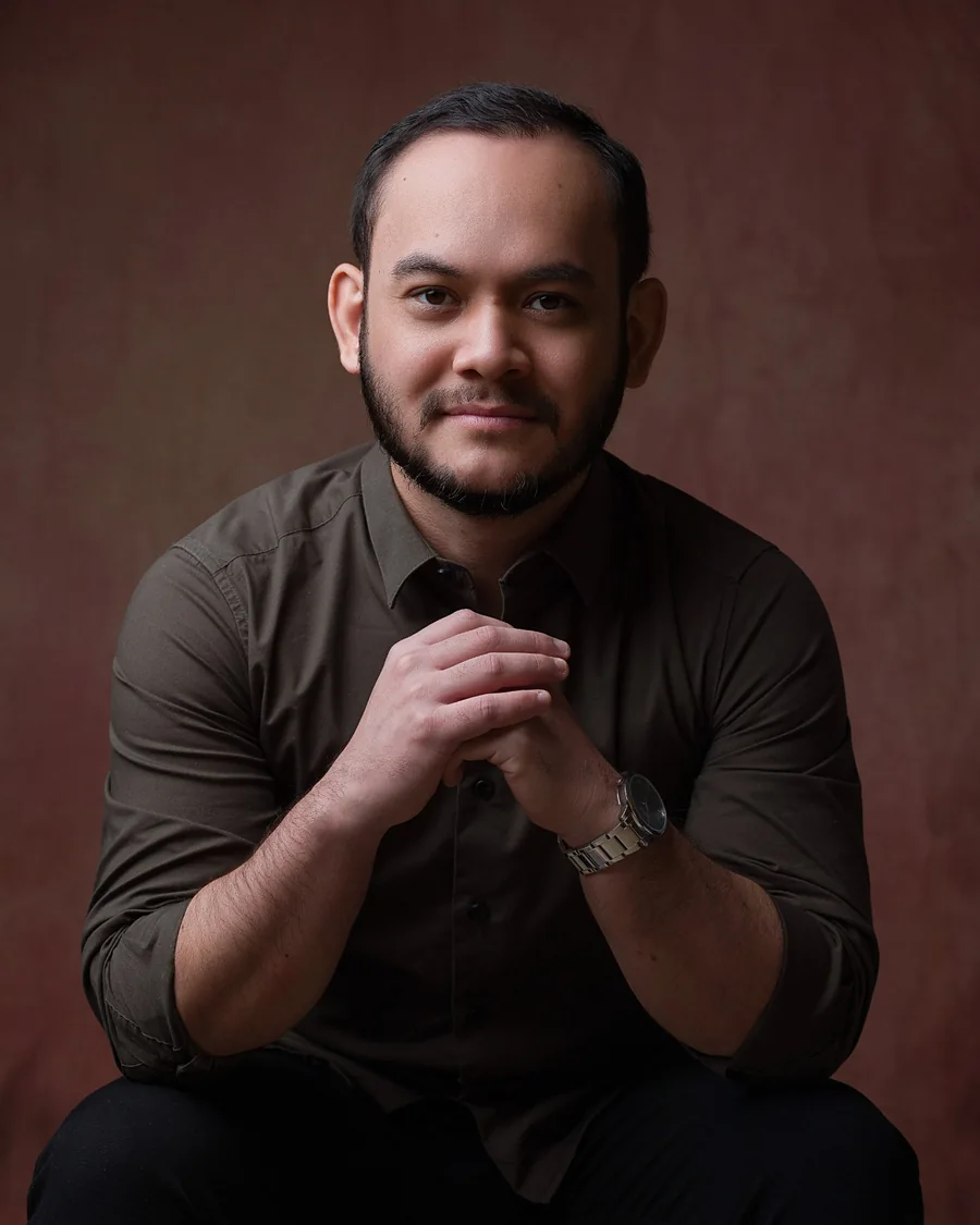 Thalles Diamantino sentado com as mãos entrelaçadas, olhando para a câmera